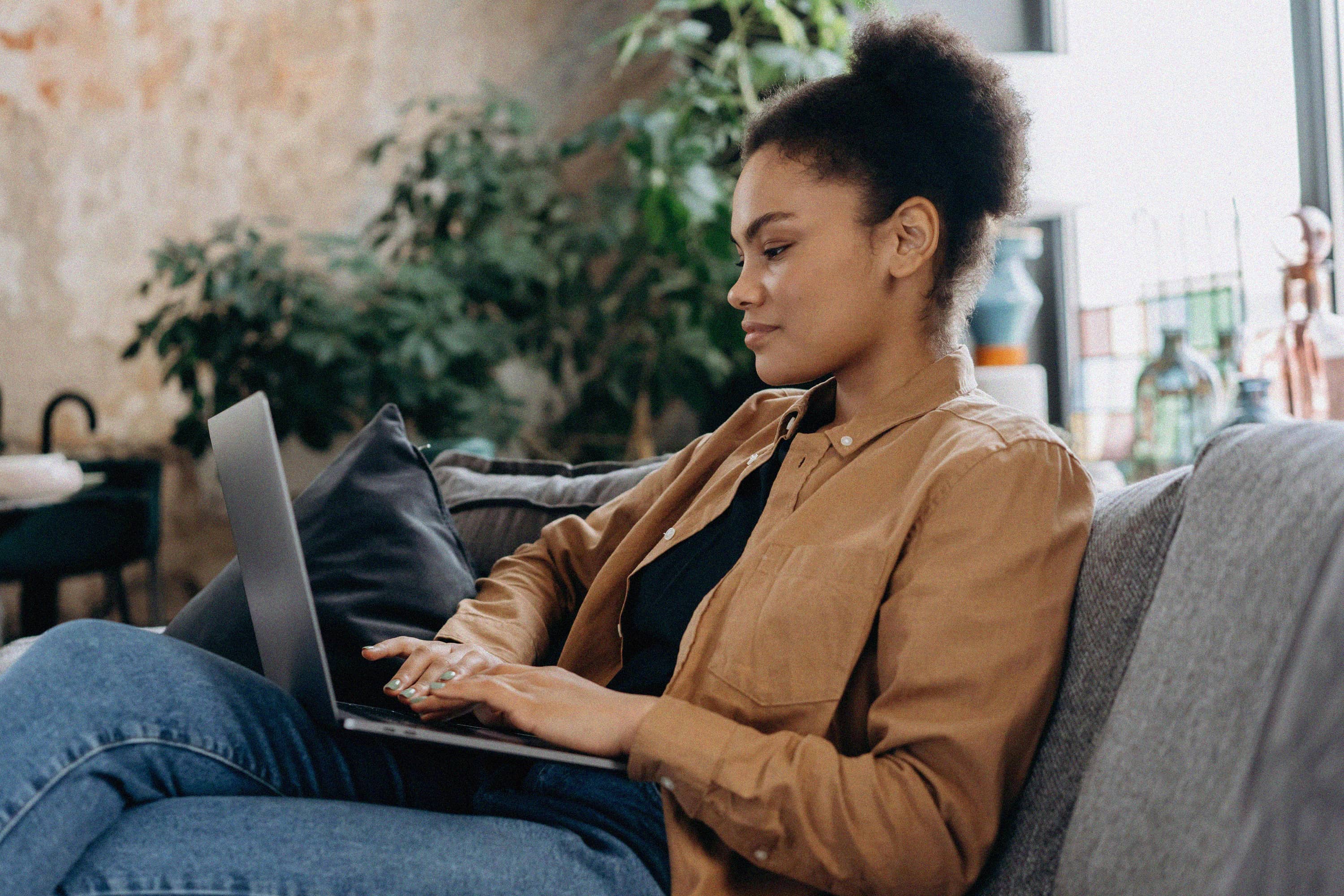 A woman using a laptop while seated on a sofa.