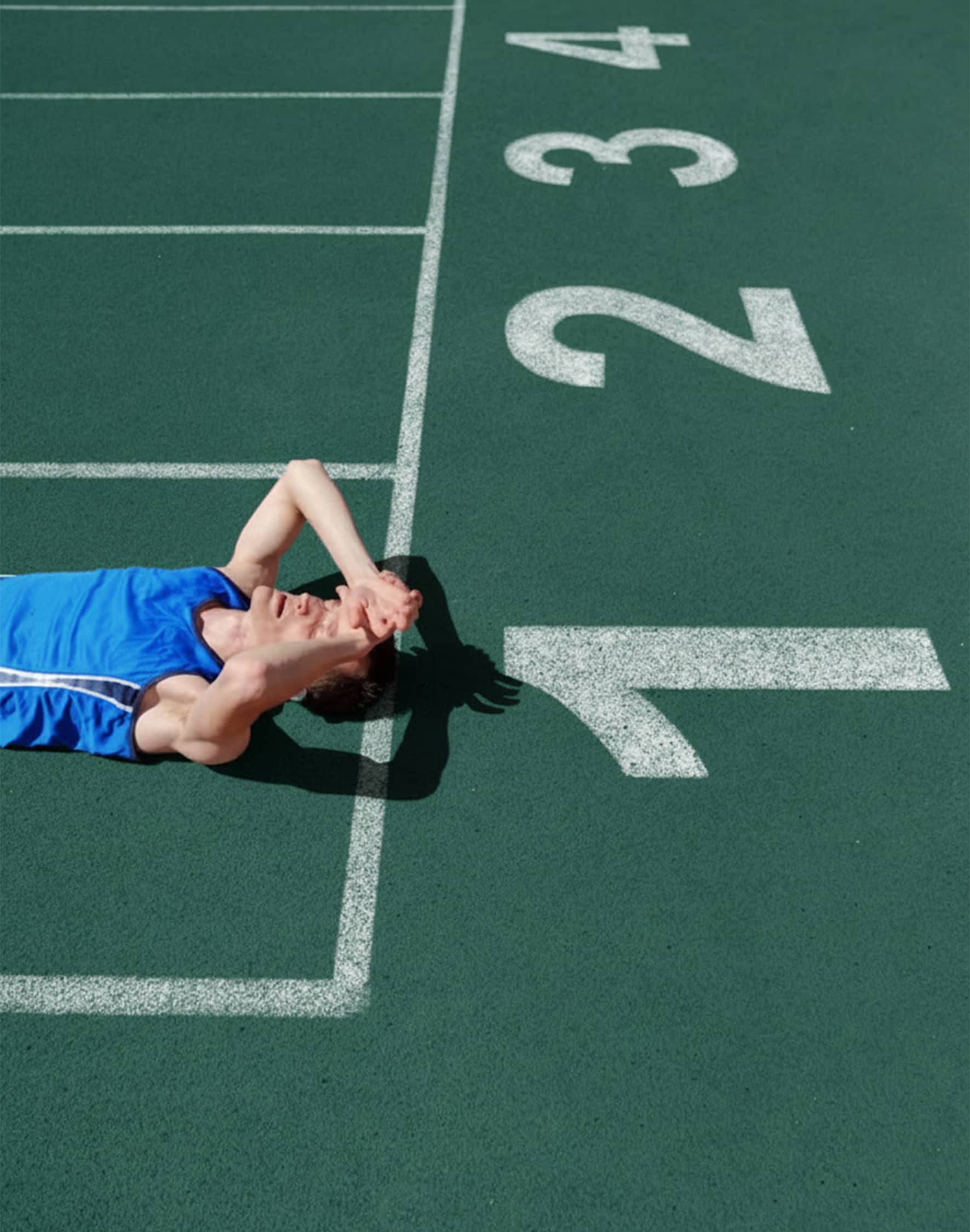 A runner resting on a green running track.