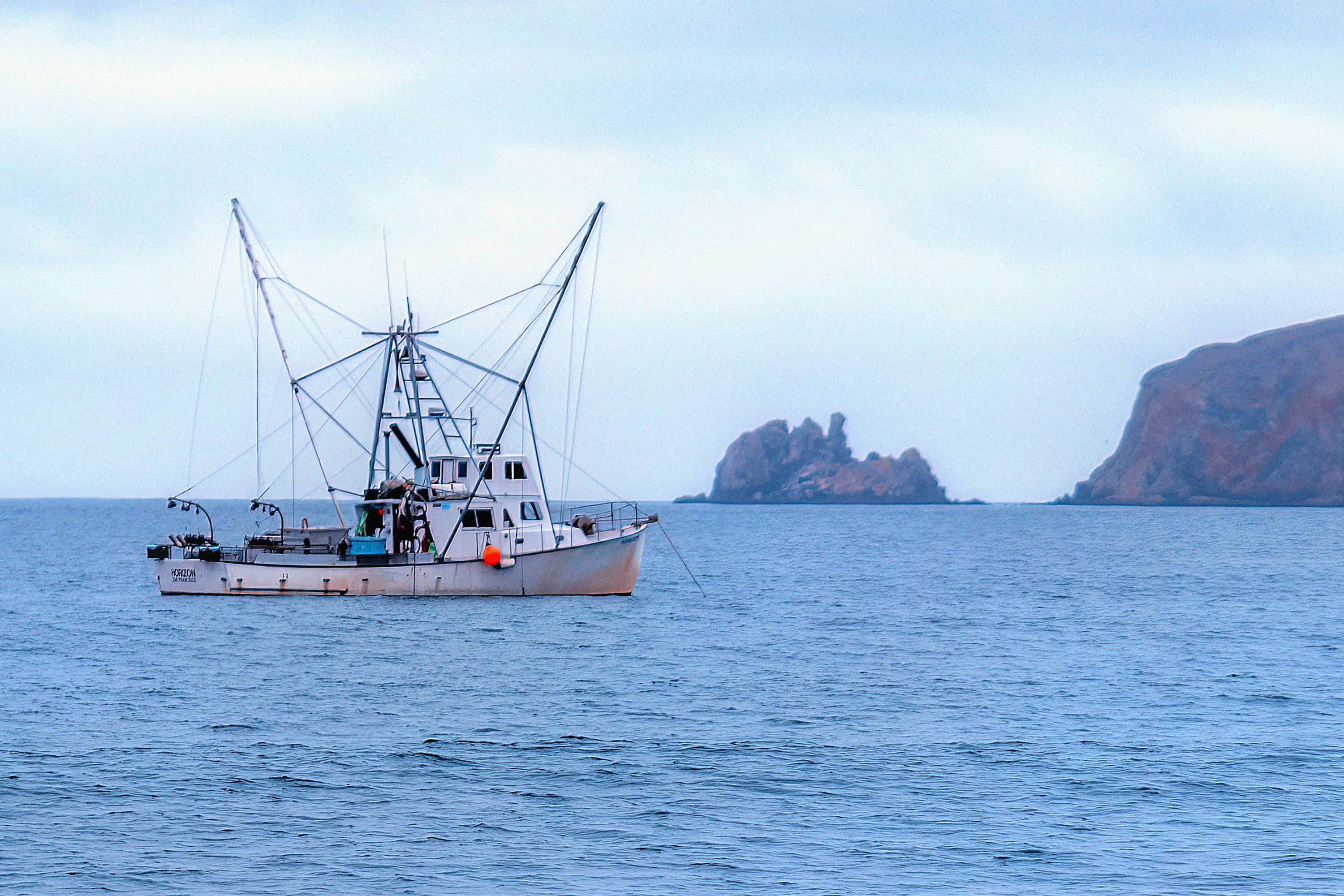 A fishing boat at sea near a rocky coastline.